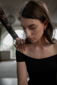 A woman in deep thought receiving comforting touch from another person, indoors, with a soft focus.